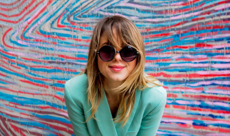 Młoda nowoczesna dziewczyna w okularach przeciwsłonecznych na tle kolorowej ściany | Hemorigen femina