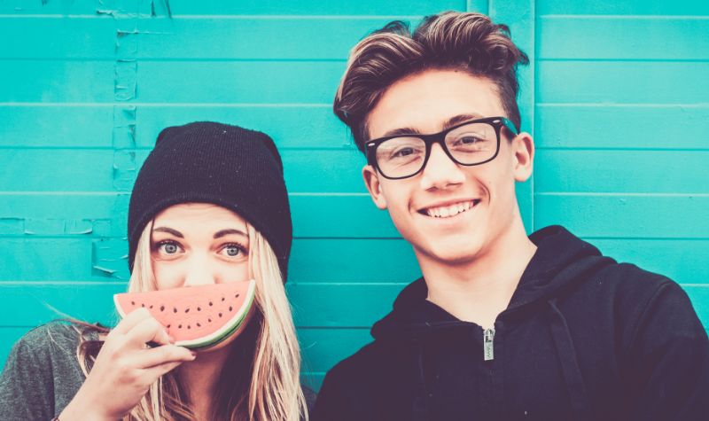 Blond nastolatka i młody chłopak uśmiechnięci na tle niebieskiej ściany | Hemorigen femina